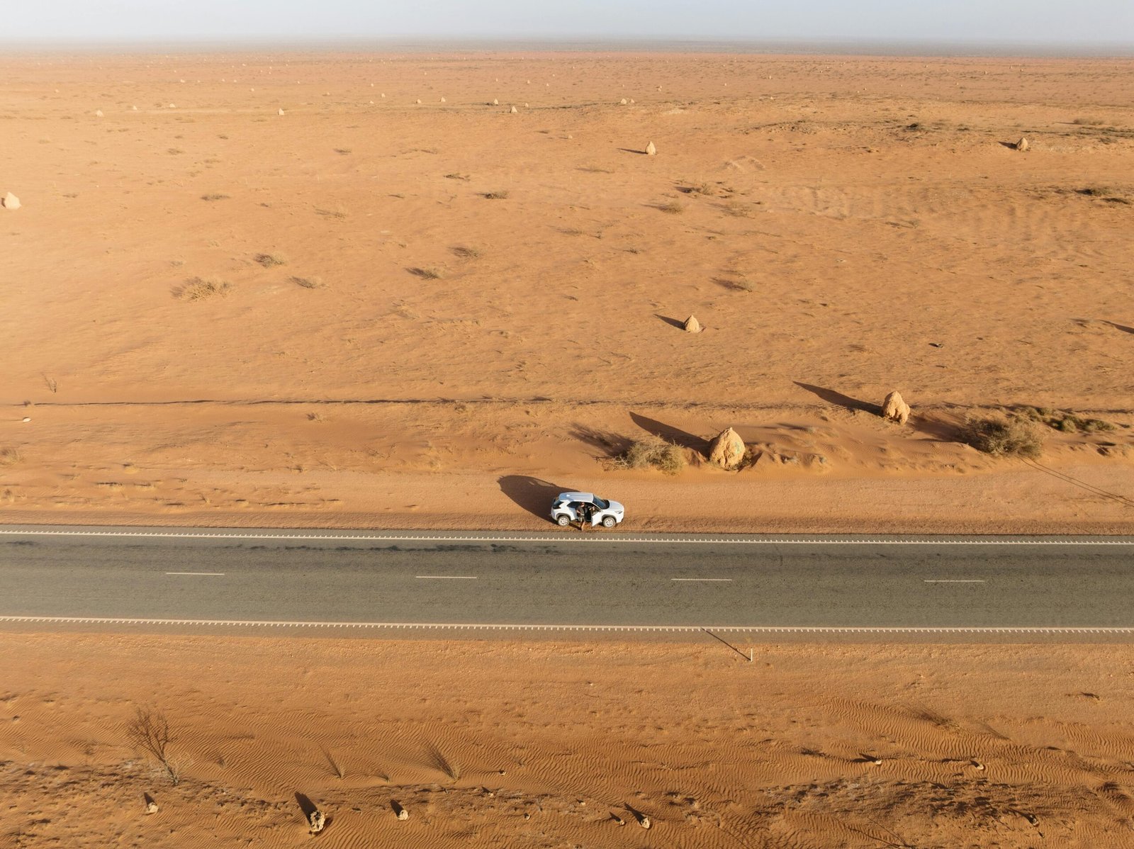 A lone car travels on a deserted road through a vast arid landscape.